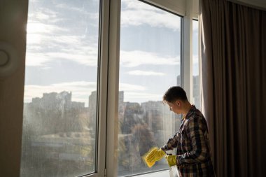 Sarı lastik eldivenli beyaz adam gündüzleri evdeki camları temizliyor. Boşluğu kopyala.