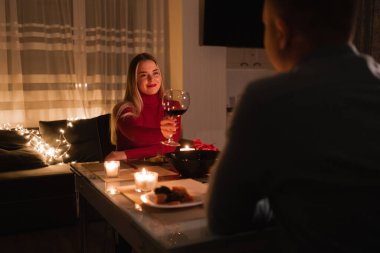 İki kişilik romantik bir akşam yemeği, evde aşık bir çift, masada şarap içen bir kadın, mum ışığında sevgililer günü, yıldönümü veya sevgililer günü kutlaması konsepti.