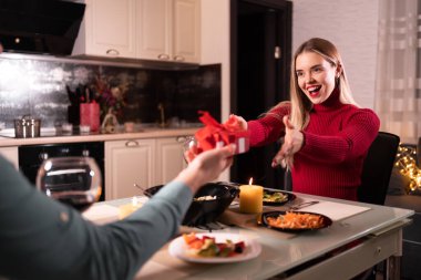 Evde iki kişilik romantik bir akşam yemeği, bir erkek bir kadına doğum günü ya da sevgililer günü hediyesi verir, akşamları mutfakta aşık bir çift, mum dolu bir masada oturur, tatil hediyesi kavramı.
