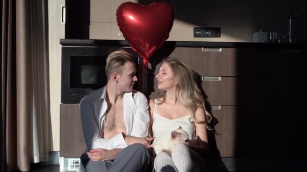 Hombre y mujer se sientan por la mañana en la cocina sosteniendo un globo en forma de corazón. concepto para celebrar el día de San Valentín, cumpleaños o aniversario. — Vídeos de Stock