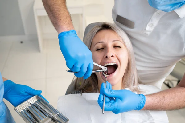 Poor girl in a patient\'s bib in a dental clinic. A dentist in blue latex gloves removes her tooth with a buccal retractor and forceps.