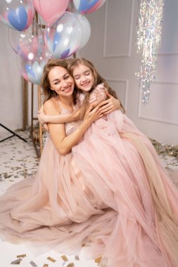 Sevimli, sevimli, neşeli, uzun elbiseli anne ve kız sarılıyorlar, tatilin tadını çıkarıyorlar, balonlar, sürpriz, hediye, gerçek tatil havası. Doğum günü, yıldönümü veya tatil konsepti