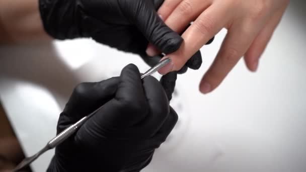 De handen van een professionele salonarbeider die een cliëntenhand vasthoudt terwijl hij een nagelriemduwer gebruikt. Manicure met behulp van nagelriemen pusher op meisjes handen. Manicure maakt een manicure in een nagel salon. — Stockvideo