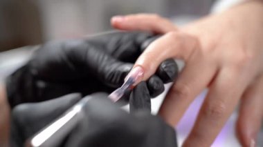 Kuaförde manikür. Tırnaklarını jöle cilasıyla kaplıyor. Yakın plan. Güzellik salonundaki kadın, pembe parıltı.