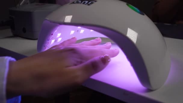 Mano femminile in lampada per unghie ultravioletta per manicure, smalto essiccante in uv, salone di bellezza. cura e manicure professionale — Video Stock