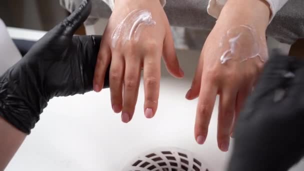 Cosmetólogo haciendo tratamientos de spa para el cuidado de las manos de una niña en un salón de belleza. La manicura frota la crema al cliente. Manicura SPA — Vídeos de Stock