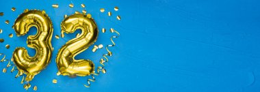 32 numaralı altın folyo balonu. Üzerinde 32 yazan doğum günü ya da yıldönümü kartı. Mavi beton arka plan. Yıldönümü kutlaması. Pankart. Boşluğu kopyala