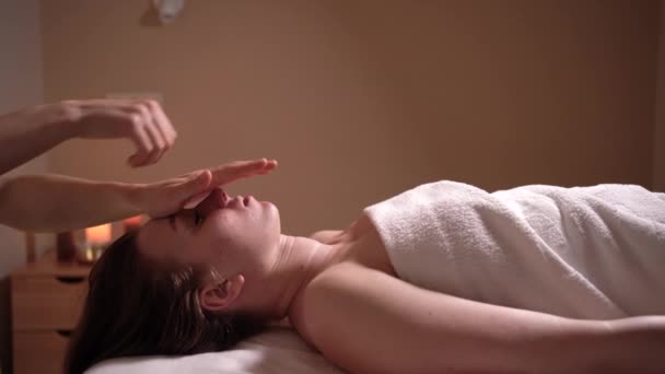 Junge attraktive hübsche Brünette bekommt eine Gesichtsmassage im Wellnessbereich. Das Konzept eines gesunden Lebensstils und der Körperpflege. — Stockvideo