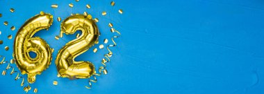 Altmış iki numaralı altın folyo balonu. Doğum günü ya da yıldönümü kartı. Altında 62 yazılıydı. Mavi beton. Yıldönümü kutlaması. Pankart. Boşluğu kopyala