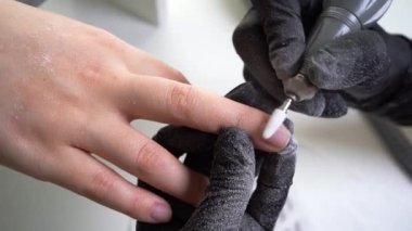 Güzellik salonunda hırdavatçı manikürü. Siyah eldivenli manikürcü kadın tırnaklarındaki eski ojelerin tırnaklarını temizlemek için elektrikli matkap kullanıyor..