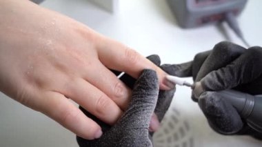 Güzellik salonunda hırdavatçı manikürü. Siyah eldivenli manikürcü kadın tırnaklarındaki eski ojelerin tırnaklarını temizlemek için elektrikli matkap kullanıyor. Krillerin kalıntıları yan tarafa uçuyor..