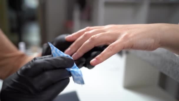 Опытный маникюрша стирает женские ногти с обезжиривателем и белой салфеткой в салоне красоты, маникюрши руки в перчатках и ногти клиентов. — стоковое видео
