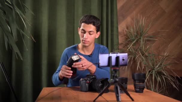 Training voor beginnende fotografen, online cursussen. Een moslim registreert een video-review van fotografische apparatuur met behulp van een applicatie op een smartphone. Basis van het werken met zaklamp met gepulseerd licht. — Stockvideo