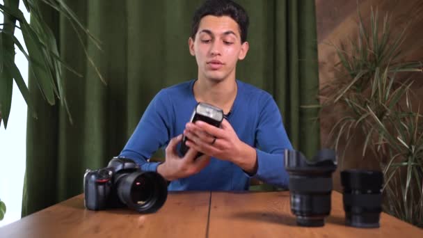 Videohandledning om hur man väljer och arbetar med en fotoblixt för en kamera. En ung attraktiv arabisk man filmar sig själv framför kameran. Online handledare, mentor. — Stockvideo