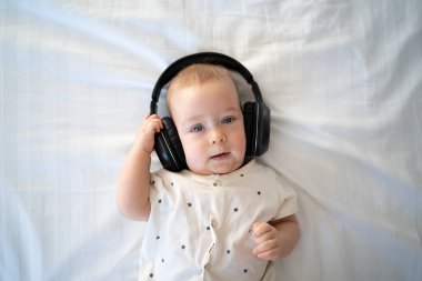 Top view, kablosuz kulaklıkla müzik dinleyen çocuk, kulaklıklı çocuk, yatakta yeni yürüyen çocuk, beyaz arka plan