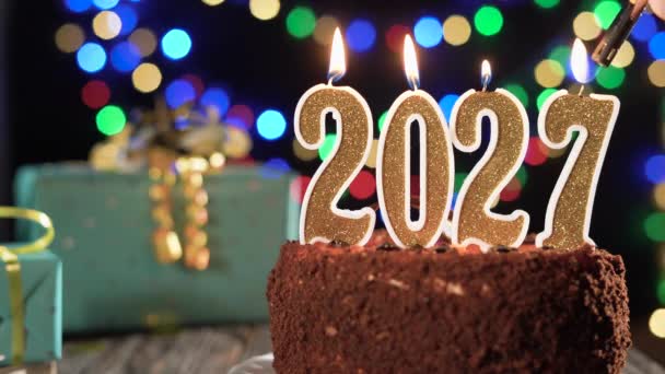 Feliz Ano Novo. vela de ouro número dois mil vinte e sete em um bolo doce sobre a mesa, 2027. Fogo do isqueiro, apaga a vela do feriado. — Vídeo de Stock