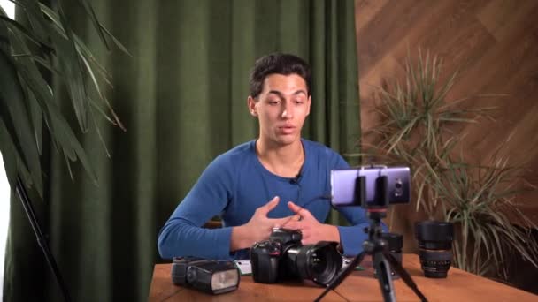 Szkolenia dla początkujących fotografów, kursy online. Muzułmanin nagrywa wideo przegląd sprzętu fotograficznego za pomocą aplikacji na smartfonie. Trzyma znak z lekcją tekstu 1 — Wideo stockowe
