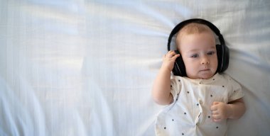 Pop müzik. Mutlu gülümseyen yeni doğmuş bebek, beyaz arka planda kulaklıkla müzik dinliyor. Neşeli çocuk portresi, küçük DJ, afiş
