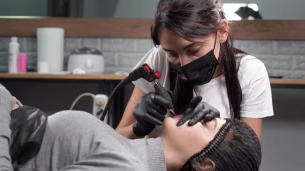 Жінка-косметолог, що застосовує постійний макіяж губ для пацієнта, татуювання забарвлення губ пігментом, робота майстра мікроблокування в салоні — стокове відео