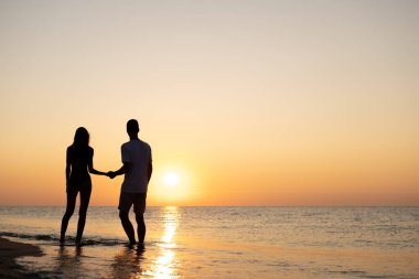 Birbirlerine aşık çiftler plajda gün batımında romantik anlar yaşarlar. Yaz tatilinde genç aşıklar. Aşk ya da balayı kavramı. Gün batımında siluet öpücüğü