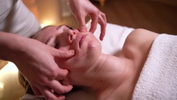 Jonge aantrekkelijke vrouw krijgt een gezichtsmassage in de spa. gezichtsbehandelingen, gezonde levensstijl en lichaamsverzorging. Langzame beweging — Stockvideo