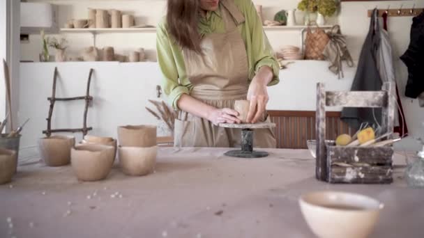 Aardewerk kunstenaars werkplek jonge vrouw staan aan een tafel in een studio werken met rauwe klei om een aardewerk vaas of pot te maken. Een kunststudent die handgemaakte keramiek beoefent in een werkplaats. — Stockvideo