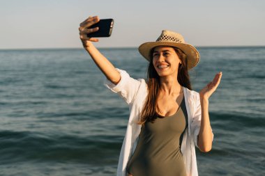 Okyanusta bir kızın yakın plan portresi. Hasır şapka takıyor, elinde bir akıllı telefon tutuyor ve akıllı telefonundaki uygulamayı kullanarak bir video görüşmesi yapıyor. ulaşılabilir internet konsepti. Pankart. Boşluğu kopyala