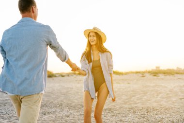 Gün doğumunda deniz kenarında kumlu okyanus açıklarında gün batımında, gün batımında gülümseyen mutlu genç çiftin yan görüntüsü. Boşluğu kopyala