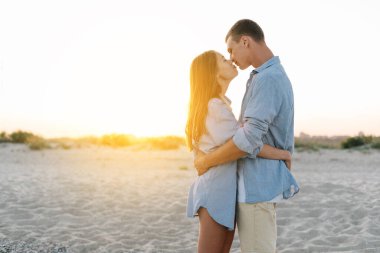 Gün batımında plajda sıradan giysiler içinde öpüşen romantik bir çift. Tropik bir tatil köyünde balayı kavramı. Pankart. Boşluğu kopyala