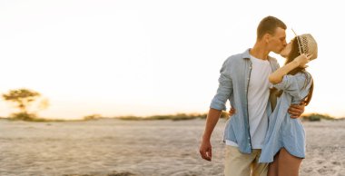 Açık havada aşık genç bir çift. Şık, genç bir moda çiftin çarpıcı şehvetli portresi, erkek ve kadın akşam günbatımında okyanus kıyısında yürürken öpüşüyor. Boşluğu kopyala