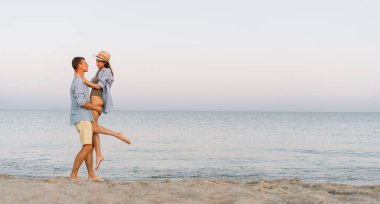 Kumsalda durup deniz manzarasının tadını çıkaran mutlu yaşlı bir çift. Genç bir adam kız arkadaşını okyanusun arka planına karşı kollarıyla kaldırır. Pankart. kopyalama alanı. Boş zaman, aşk konsepti