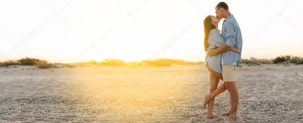 romantic couple on the beach in casual clothes kissing at sunset. The concept of a honeymoon at a tropical resort. Banner. copy space