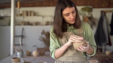 Güzel genç bir kadın, bir kase işlenmemiş kilden bir parça tutuyor tarak, düzleştiriyor, şekillendiriyor ve yontuyor. Kadın atölyede duruyor ve kilden bir tencere yapıyor.