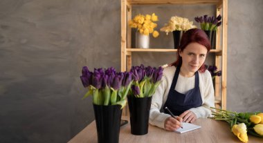 Avrupa çiçek dükkanı konsepti. Çiçekçi bir kadın elinde bir kalemle masada oturuyor ve çiçekçi dükkanına çiçek ve çiçek teslimatı için talepte bulunuyor. Boşluğu kopyala.