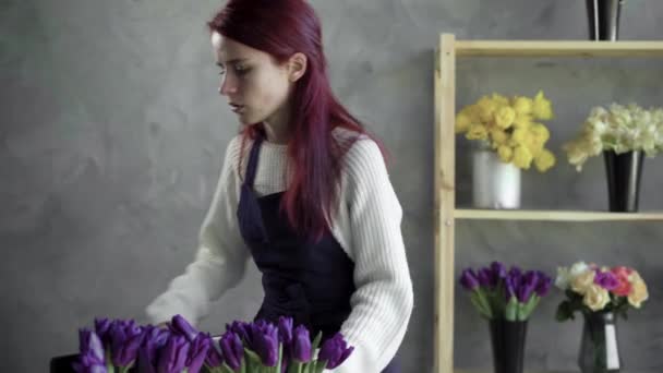 Empresário florista mulher em um avental compõe um buquê de tulipas, gradualmente adicionando flores de cores diferentes para ele. — Vídeo de Stock