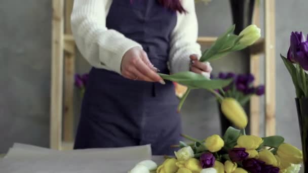 Las manos de una florista femenina en un delantal que trabaja en su propia florería. una mujer recoge un hermoso ramo de tulipanes amarillos. — Vídeos de Stock