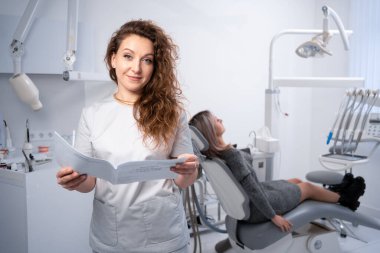 Klinikteki kadın dişçinin portresi. Diş kliniği ve oral sağlık konsepti. Müşteri kartı olan bir doktor kameraya bakar. Boşluğu kopyala.