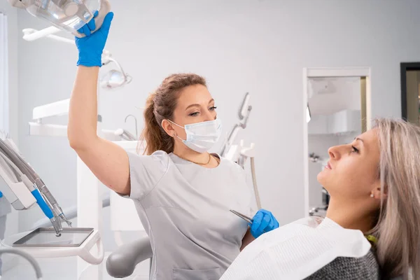 Woman dentist in the dental office preparing for treatment turns on the light and prepares the equipment. copy space.