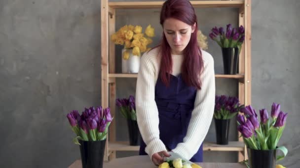 Флорист в фартуке на работе красивая молодая леди делает модный современный букет тюльпанов. Рабочее место флориста. Готовлю подарок для любимого человека. Весенний цветок. — стоковое видео