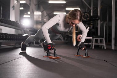 Spor tişörtlü güzel bir fitness kızının şınav çekerken yakın çekimi. Spor salonunda antrenman yapıyor. Boşluğu kopyala.