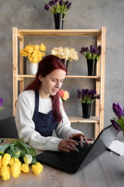 Çiçekçi dükkanında çalışan bir çiçekçinin portresi. Lojistik ve teslimatı organize etmek için dizüstü bilgisayar kullanıyor. İnternetten sipariş alıyor..