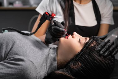 Güzellik salonunda dudaklarında kalıcı makyaj yapan genç bir kadın. Üstat pigmenti yüze uygular.