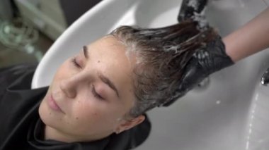 Güzel bayan rahatla ve saçını şampuan ve masajla yıkarken rahatla. Şık saç stili, güzellik ve moda konsepti olan kuaför salonu..