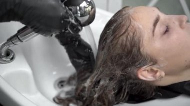 Eldiven giymiş bir kuaförün elleri müşterinin kafasını yıkar. Güzel bayan rahatla ve saçını şampuan ve masajla yıkarken rahatla..