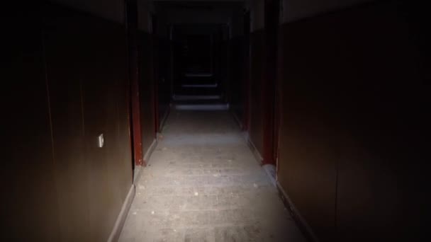 Homem com uma lanterna caminha ao longo do corredor arruinado de um edifício do hotel ou de um edifício de vários andares. Tiroteio POV — Vídeo de Stock