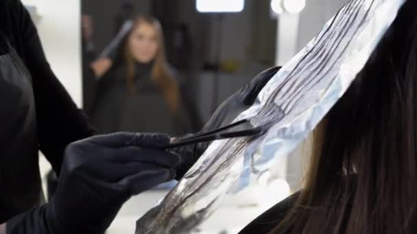 Vue latérale rapprochée d'une mèche de cheveux féminins sur une feuille spéciale de papier d'aluminium, le maître applique une teinture capillaire avec un pinceau. Le processus de mise en valeur par un maître professionnel dans un salon de beauté. — Video