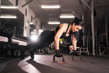 Siyah spor bluzu ve tayt giymiş güzel bir atletik kızın yan görüntüsü spor salonunda yoğun bir idman sırasında şınav çeker. Sağlıklı yaşam tarzı, jimnastik konsepti, kopyalama alanı