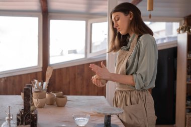 Kadın sanatçı ile yaratıcı dikiş işi yapan kadın çanak çömlek şekillendirme ve el oymacılığı için araç kullanıyor. Çömlekçinin el işi çömlek yapmak için hammaddelerle çalıştığı atölyedeki çalışma masası.