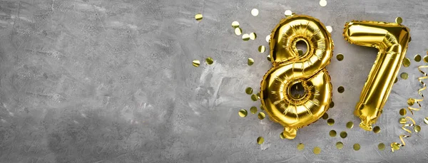 Sarı folyo balon numarası, beton zemin üzerinde 87 numara. 87 yazısıyla birlikte tebrik kartı. Yıldönümü konsepti. Yıldönümü, doğum günü, yeni yıl kutlaması için. afiş, boşluğu kopyala.