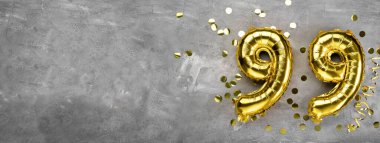Beton arka planda 99 numaralı sarı folyo balonu. 99 'un yazılı olduğu tebrik kartı. Yıldönümü konsepti. Yıldönümü, doğum günü, yeni yıl kutlaması için. afiş, boşluğu kopyala.
